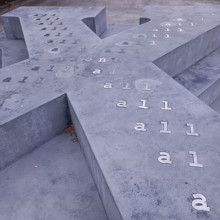 Monument i betong i form av bokstaven X liggande med text på