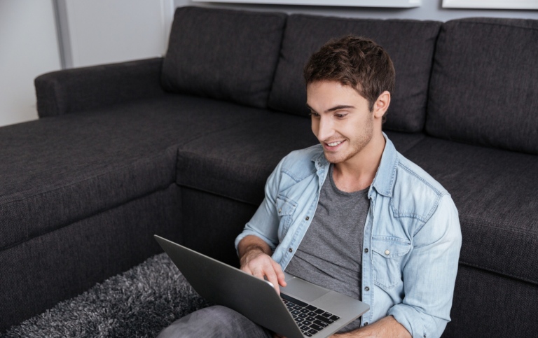 Glad kille med laptop i hemmamiljö. Foto: Mostphotos