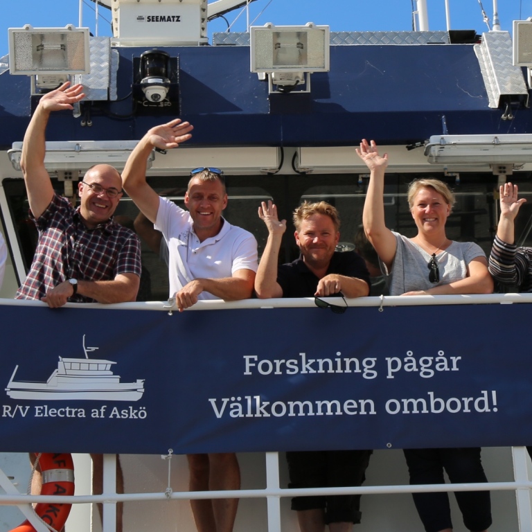 Flera medarbetare från Östersjöcentrum står på fartyget Electra och vinkar till kameran.