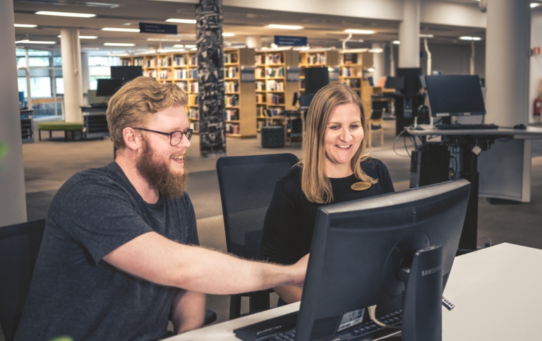 Two persons looking at a computer screen, bookshelves in the background. Photo Karl Edqvist