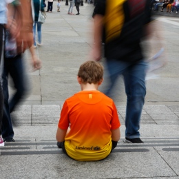 A child is sitting on the sidewalk while adults pass by