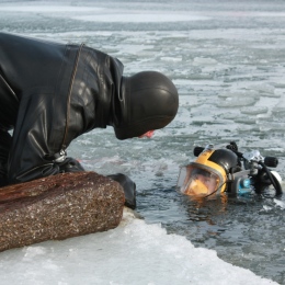 En dykare på land pratar med en dykare som sticker upp huvudet ur vattnet.