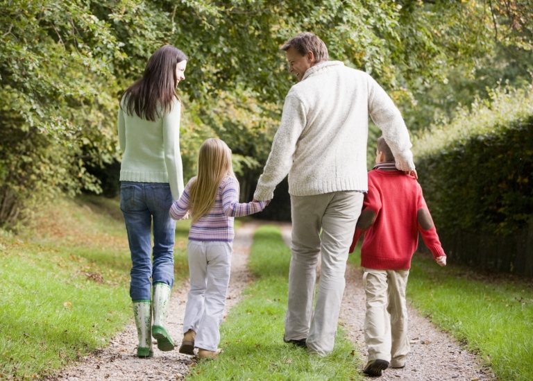 En familj går på promenad i skogen och håller varandra i handen