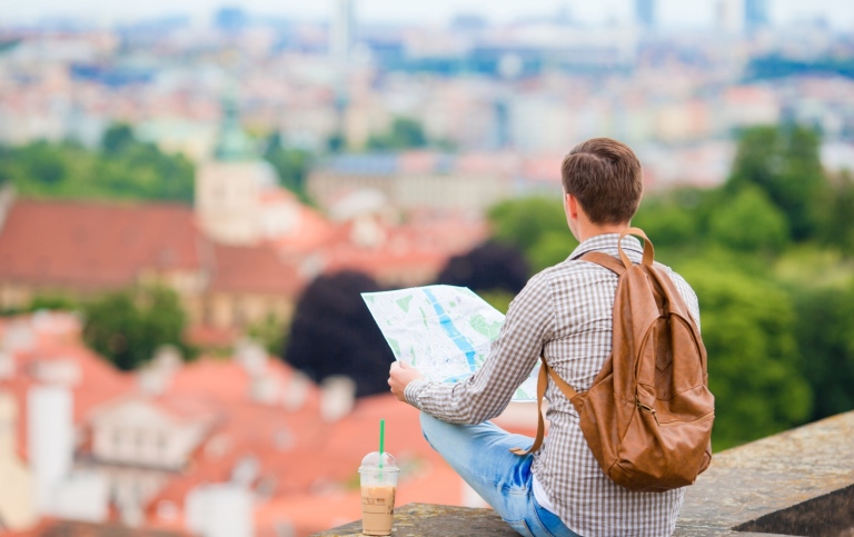 En ung kille med ryggsäck och karta tittar ut över en stad.