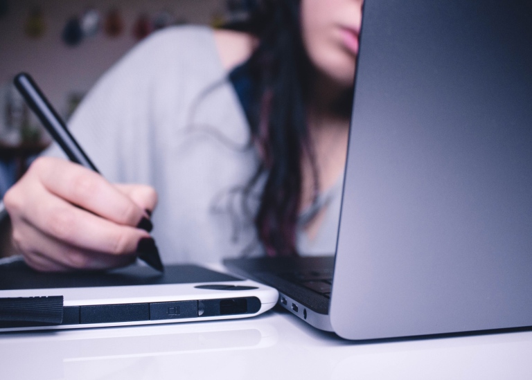 Genrebild distansstudier: En kvinna sitter och jobbar med dator och skrivplatta.