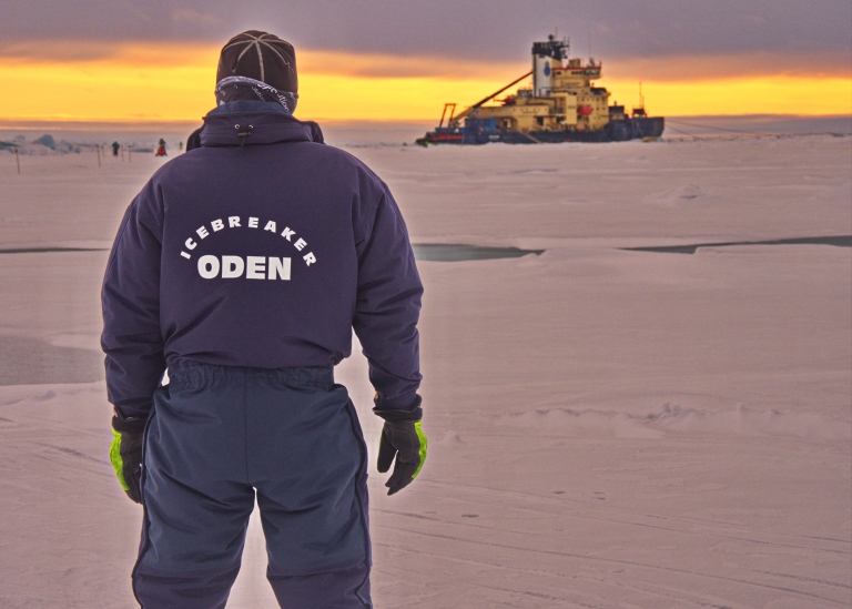Forskare står på isen med isbrytaren Oden i bakgrunden