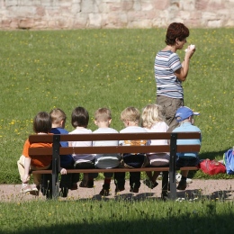 Förskolebarn sitter på en bänk med sin lärare