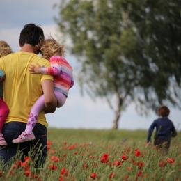 En pappa bär två barn över ett fält