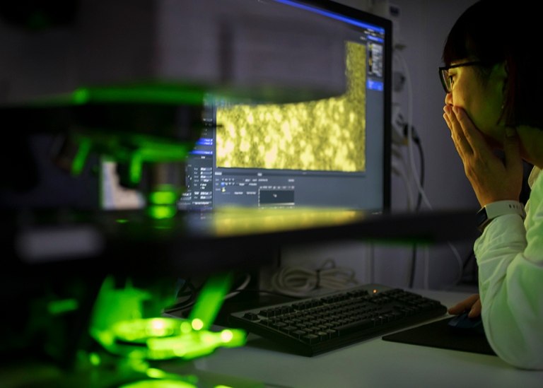 Forskare sitter i mörkt rum med lysande grönt mikroskop