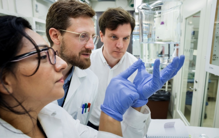 Tre forskare i labbet, tittar på glaskolv