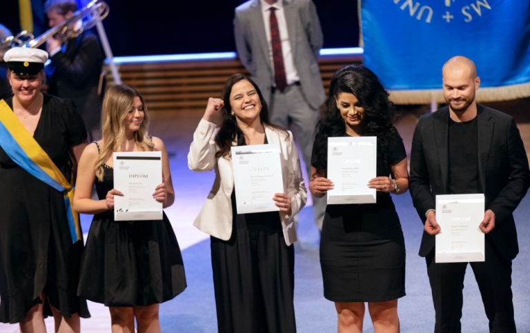 Four master students om stage with diplomas in their hands.