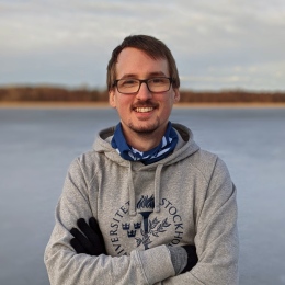 Portrait photograph of Simon Larsson, wearing a Stockholm University hoodie, taken by a frozen lake.