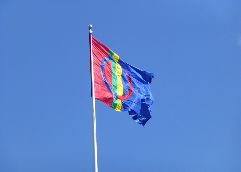 Saemien saevege - Samiska flaggan på flaggstång mot blå himmel