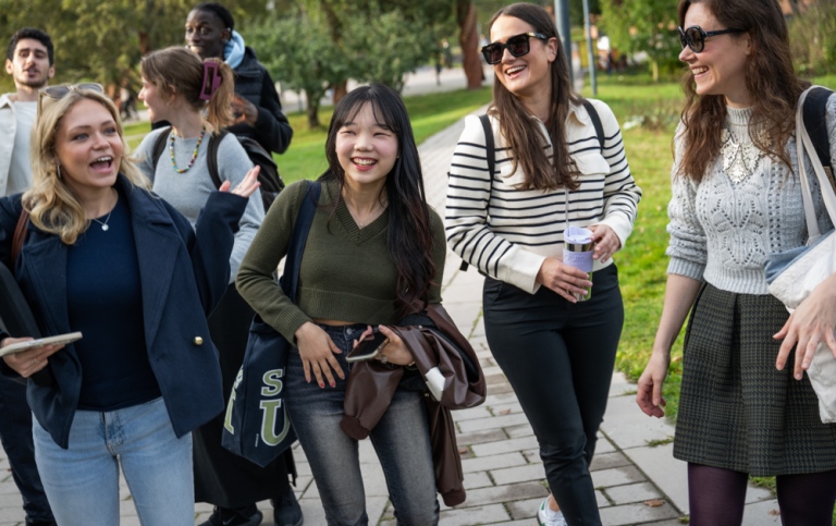 Studenter promenerar utomhus, pratar och skrattar.