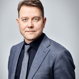 Porträttbild av Emil Elgebrant, i grå kavalj, slips och svart skjorta
