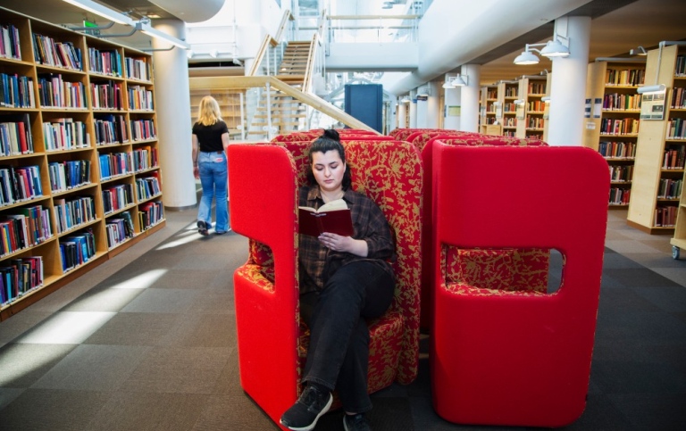 En student/besökare i en av de röda fåtöljerna på Stockholms universitetsbibliotek