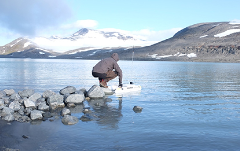 man holding a robot remote vessel in the water, with an arctic view in front of him