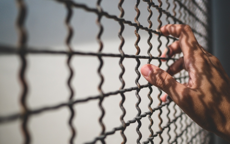 Hand of prisoner holding rustic metal fence