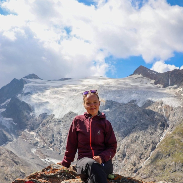 Mikaela sitter på en klippa uppe i österrike alperna med en glacier i bakgrund