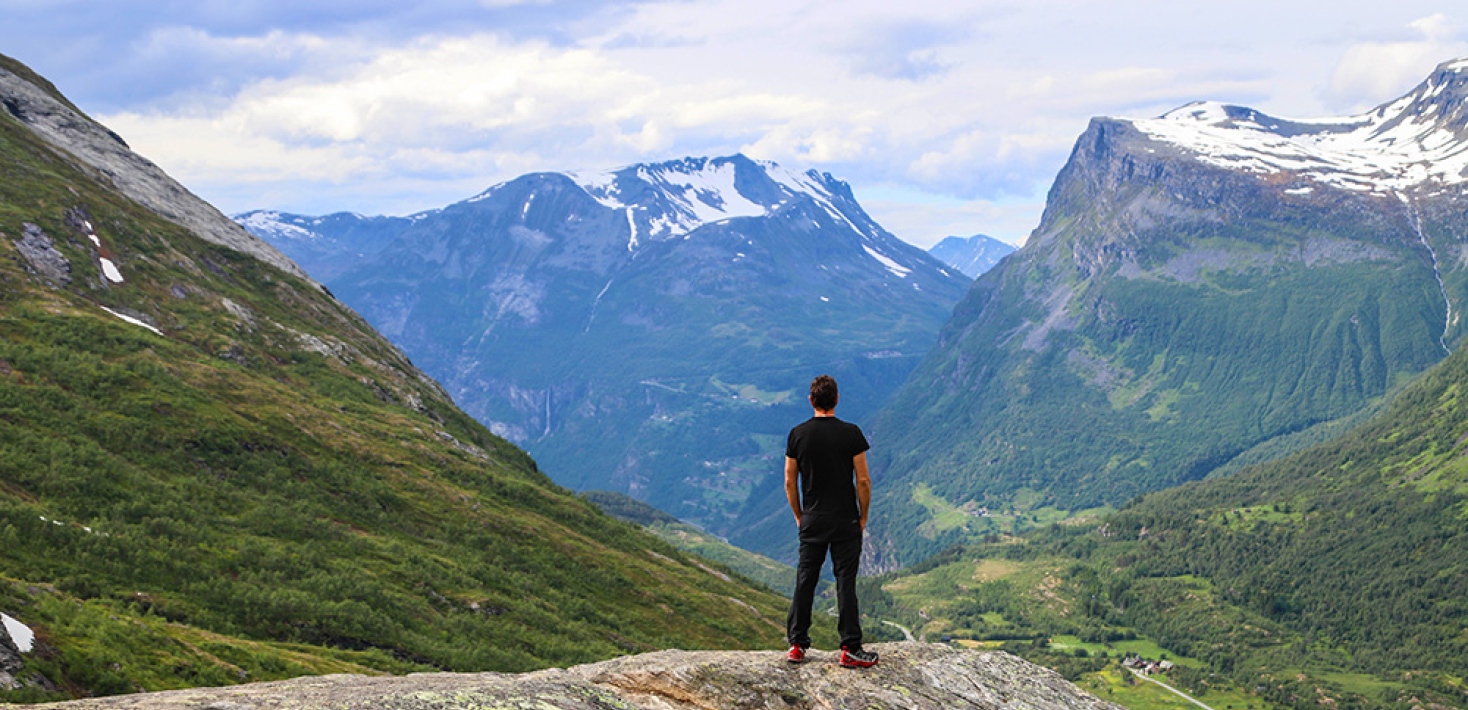 person står och tittar ut över berglandskap i Geiranger, Norge. Foto: Michael Erhardsson, MostPhotos