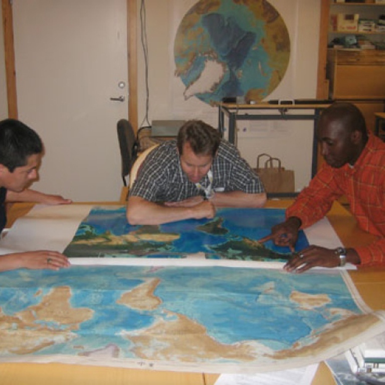 3 personer sitter och tittar på en världkarta