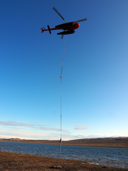 Helicopter holding a corer on a rope over the lake