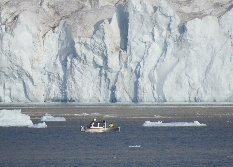 small research boat in front of glacier