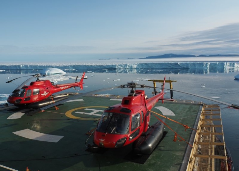 two helicopters on icebreaker Oden, on the background floating huge icebergs
