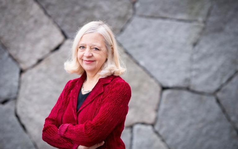 Karin Helander. Foto: Eva Dalin. Karin Helander. I bakgrunden en murad stenvägg i grått.
