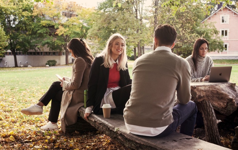 Foto på studenter som sitter på en bänk i campus Frescati då det är hösten.