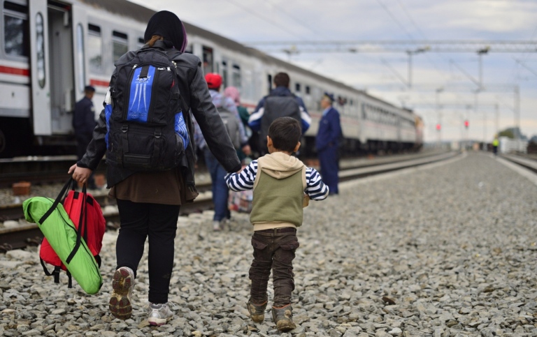Liten pojke går vid ett tåg och håller sin mamma i handen. Migranter.