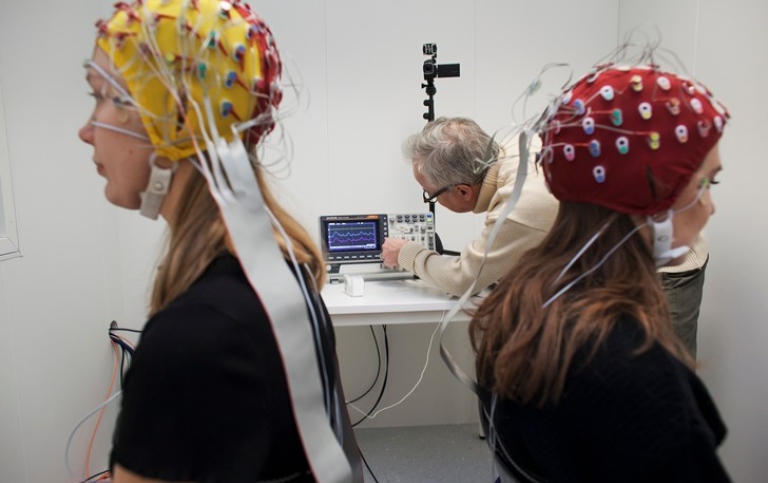 Two students woth caps with electrodes. A researcher in the background