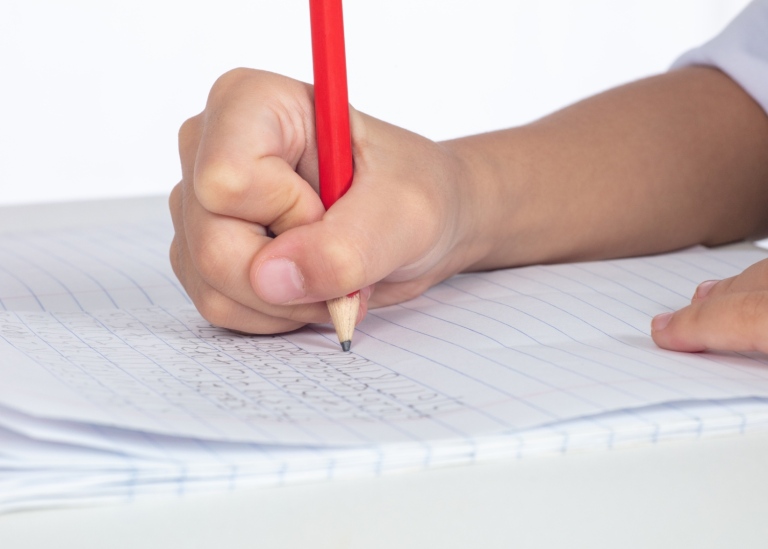 Barnhand skriver med blyertspenna på papper