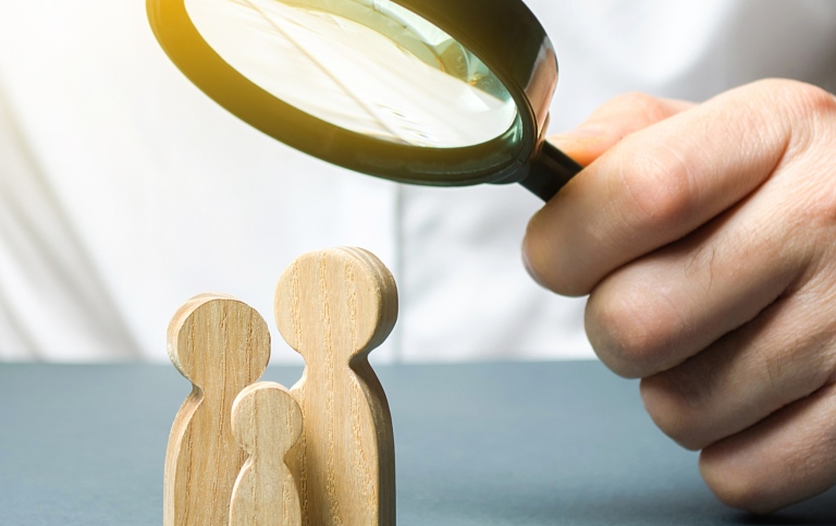 A man looks at wooden family figures under a magnifying glass.