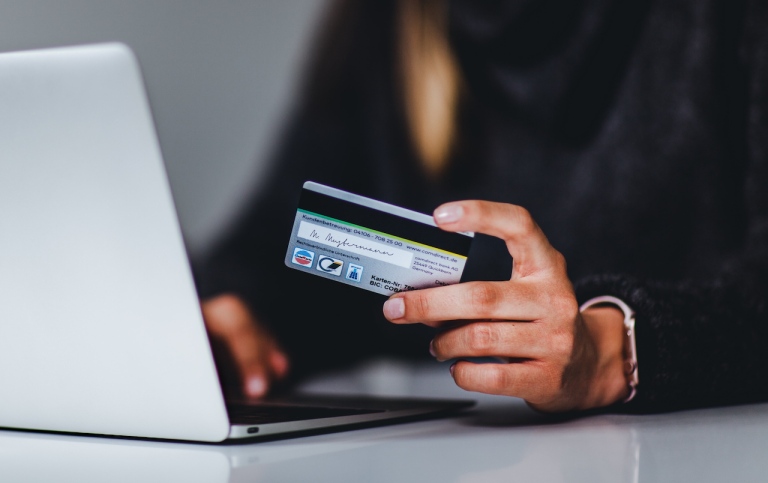 E-handel: en person sitter framför en dator med sitt bankkort i handen.