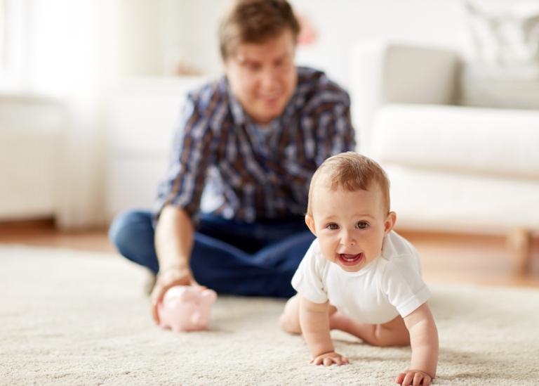 Spädbarn kryper på matta med förälder i bakgrunden. Foto: Mostphotos