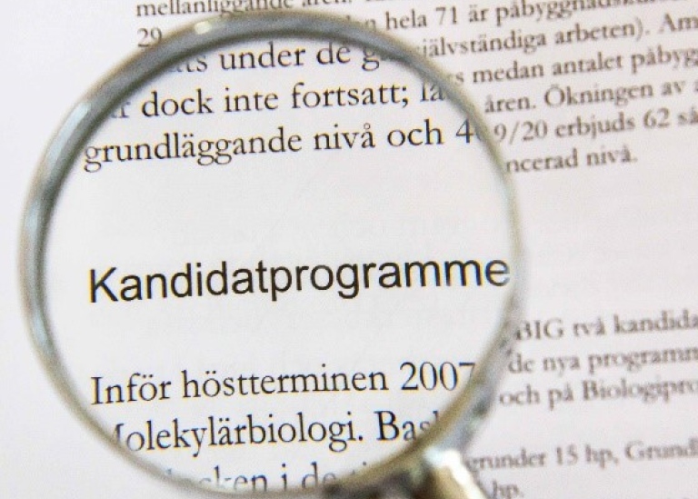 Förstoringsglas med text i bakgrunden, texten som förstoras läser "Kandidatprogrammen".