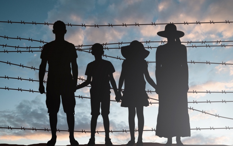 Familj med immigranter som står vid ett staket