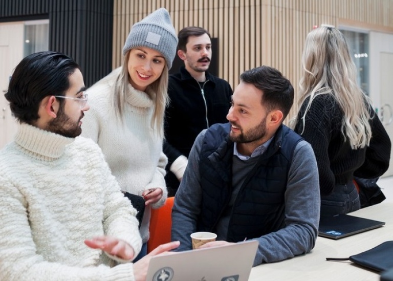 A group of students chatting in front of a laptop.