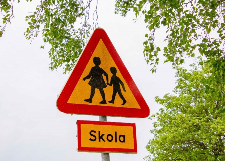 Traffic sign warning triangle with two children, below a sign saying "School" (in Swedish)