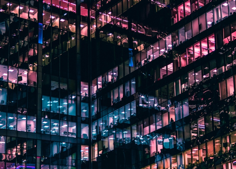 Genre photo: Office building with many floors, rooms lit in different colors. Illustrates research. 