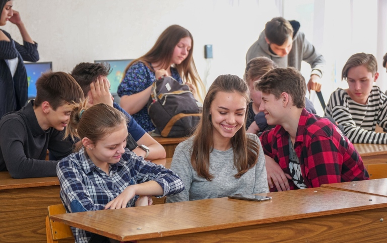 Elever vid sina bänkar i klassrum skrattar och ler tillsammans över något.