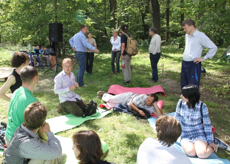 Grupp av människor sittande i skog, ser ut som att de lär sig något tillsammans.