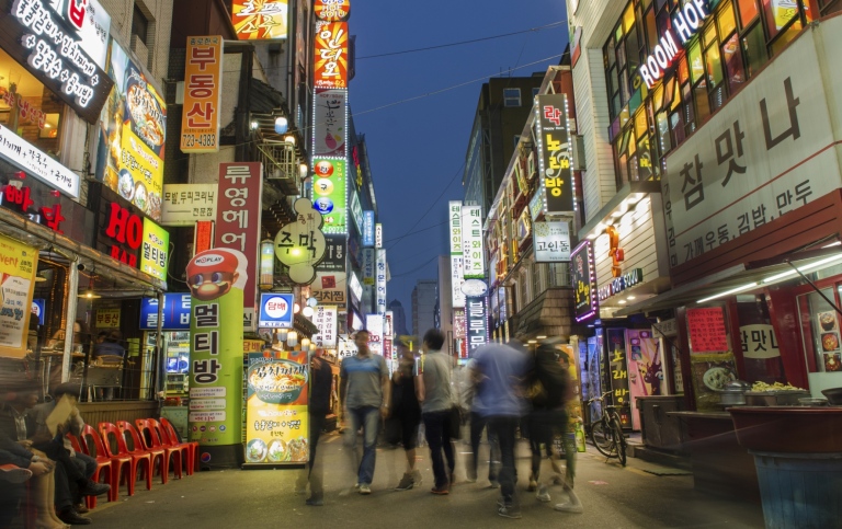 En koreansk storstad på kvällen, med lysande skyltar och människro på en gågata