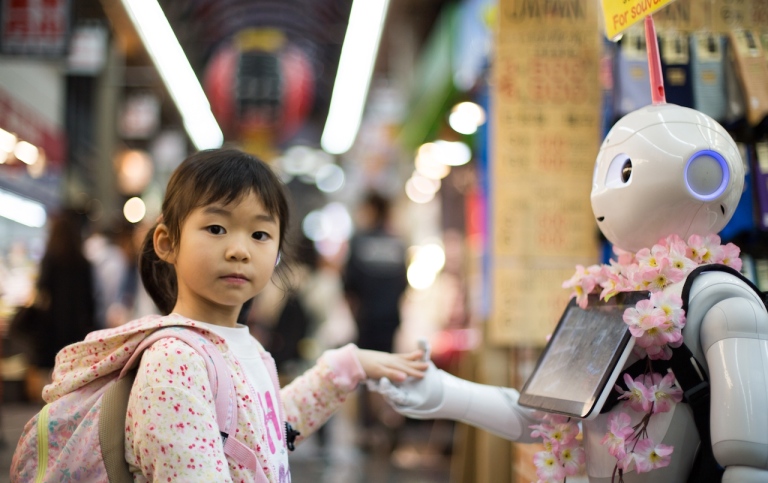 Genrebild: Ett barn och en robot håller varandra i händerna. Foto: Andy Kelly/Unsplash.