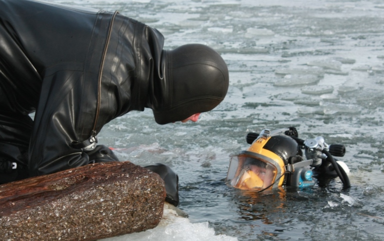 En dykare på land pratar med en dykare som sticker upp huvudet ur vattnet.