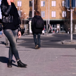 Young female in leather jacket is smoking on an empty town square.