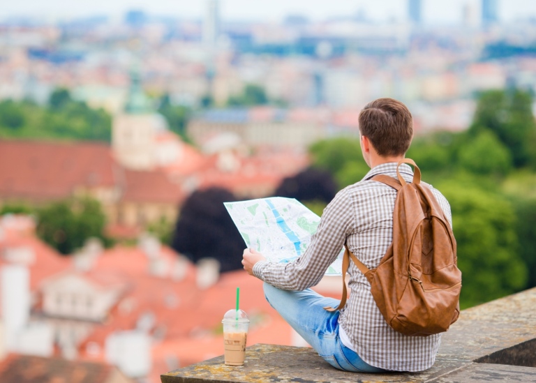 En ung kille med ryggsäck och karta tittar ut över en stad.