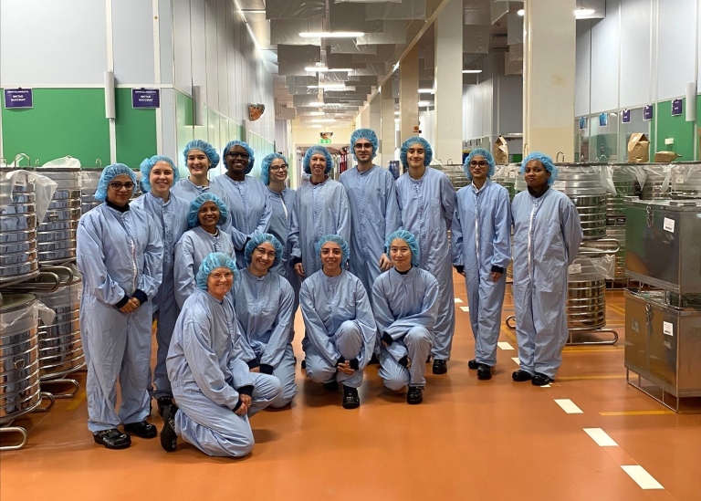 Gruppbild av femton personer i blå overall och hårskydd i fabrikslokal