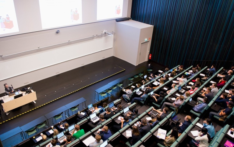 A lecture hall in a higher education, filled with students listening to a lecture
